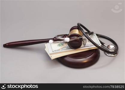 Stethoscope with judge gavel and dollar banknotes on gray background