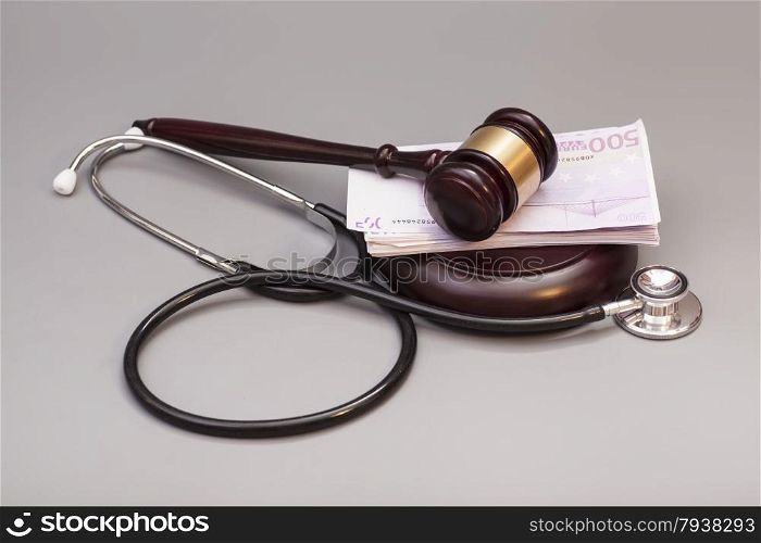 Stethoscope with judge gavel and euro banknotes on gray background