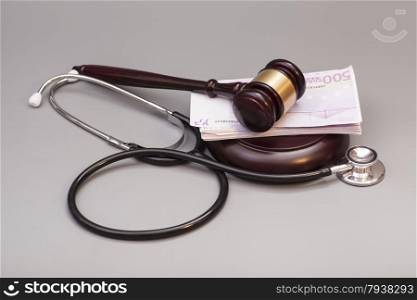 Stethoscope with judge gavel and euro banknotes on gray background