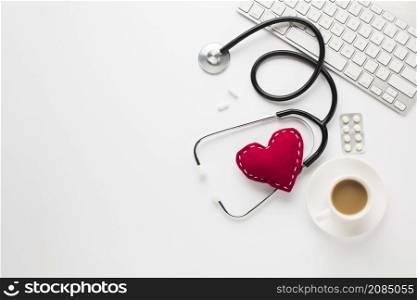 stethoscope with red heart near medicines cup coffee keyboard white desk