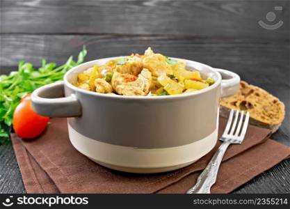 Stew of chicken breast, tomatoes, stalked celery, carrots, green peas and onions in a tureen on a napkin on black wooden board background