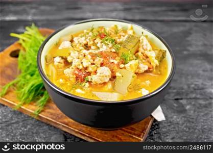 Stew of zucchini, minced chicken and tomatoes with herbs in a bowl on wooden board background
