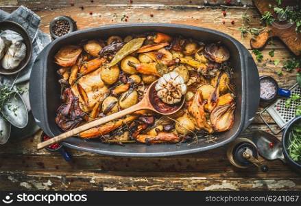Stew with roasted vegetables, forest mushrooms and wild hunting fowl in cooking pot with wooden spoon. Rabbit ragout on rustic aged background with spoons,plates and fresh seasoning, top view