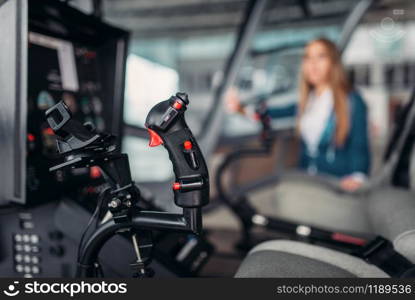 Stewardess in suit poses in helicopter in hangar, view from cabin. Air hostess in uniform near copter. Private airline. Stewardess poses in helicopter, view from cabin