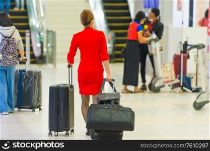 Stewardess or flight attendant woman in red uniform and mask with luggage in airport during coronavirus quarantine