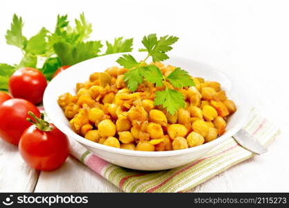 Stewed chickpeas with celery, tomatoes, onions, carrots and garlic in a plate on a towel on wooden board background