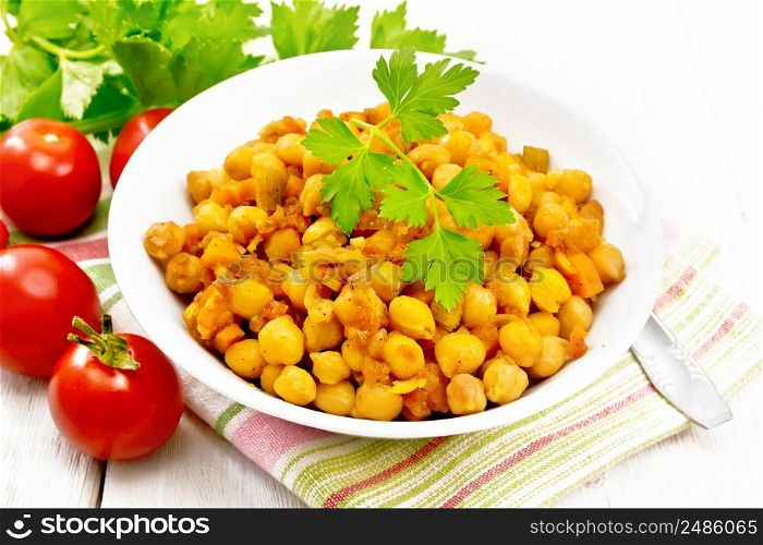 Stewed chickpeas with celery, tomatoes, onions, carrots and garlic in a plate on a napkin on wooden board background