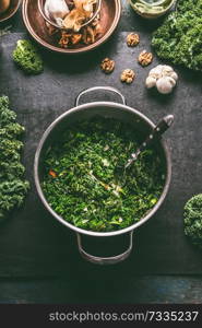 Stewed kale in cooking pot on dark kitchen table background with ingredients, top view