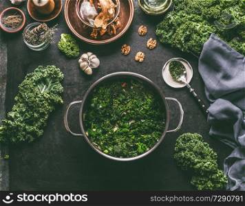 Stewed kale in cooking pot on rustic kitchen table with ingredients for vegan kale recipes: nuts,garlic, olives oil, top view. Healthy meal.  Detox vegetables .  Clean eating and dieting concept.