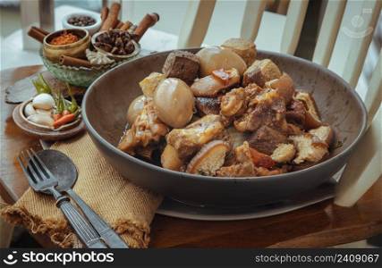 Stewed pork leg, Boiled eggs and Tofu in ceramic bowl served with Garlic and spoon and fork on wooden background. Selective focus.