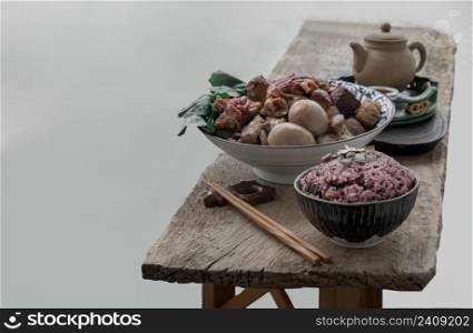 Stewed pork leg, Boiled eggs, Tofu and Kale in ceramic bowl served with Riceberry rice and Chinese tea on old wooden table. Copy space, Selective focus.