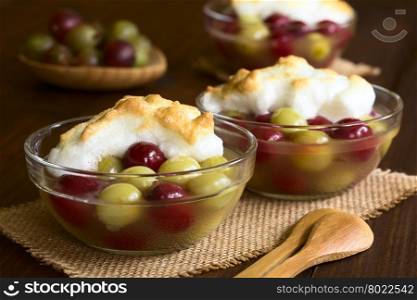 Stewed red and green gooseberry dessert with meringue in glass bowls, photographed with natural light (Selective Focus, Focus on the front of the meringue in the first bowl)