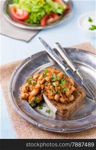 Stewed white beans in tomato sauce on toasted bread, selective focus