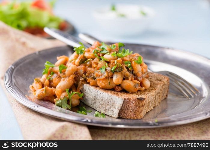 Stewed white beans in tomato sauce on toasted bread, selective focus, closeup
