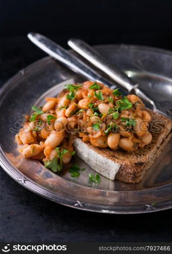 Stewed white beans in tomato sauce on toasted bread, selective focus, closeup
