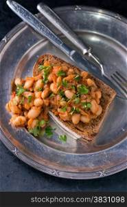 Stewed white beans in tomato sauce on toasted bread, selective focus, closeup, top view
