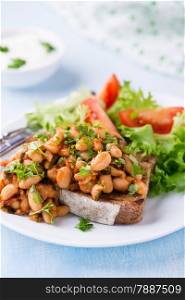 Stewed white beans in tomato sauce on toasted bread with green salad, selective focus