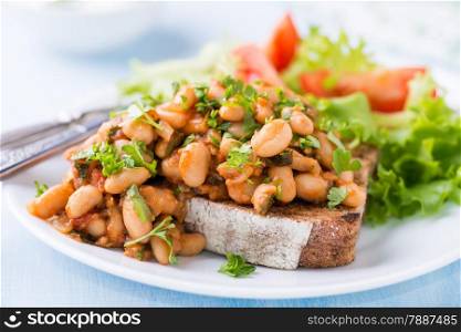 Stewed white beans in tomato sauce on toasted bread with green salad, selective focus, closeup