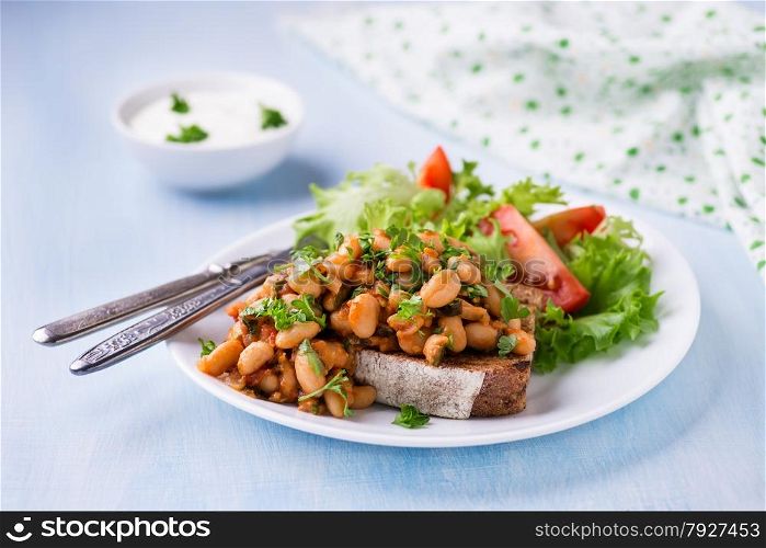 Stewed white beans in tomato sauce on toasted bread with salad, selective focus