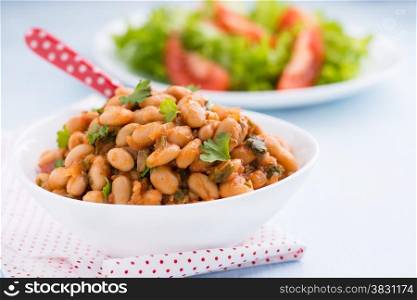 Stewed white beans with tomato sauce and parsley in white bowl, close up, selective focus
