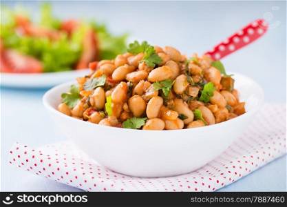 Stewed white beans with tomato sauce and parsley in white bowl, close up, selective focus
