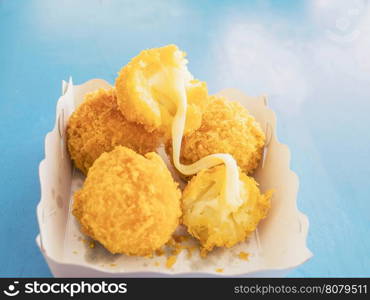 Sticky stretch cheese balls in paper container over blue table background