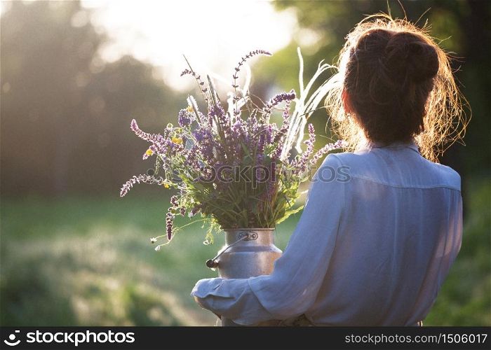 still life - girl in the village works in the garden. girl holds a Milk churn with wild flowers. in sunset light