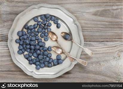 Still life in the old style with blueberry and silver tableware on the background of old boards