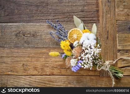 Still life of bouquet of dried flowers with orange segment on wooden background