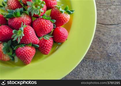 still life of fresh red strawberries on green dish over wooden background. red strawberries