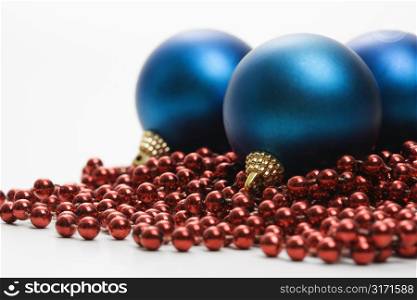 Still life of large blue Christmas ornaments and strings of red beads.