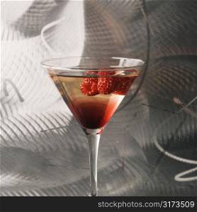 Still life of martini mixed drink with raspberry fruit agaisnt textured metallic background.