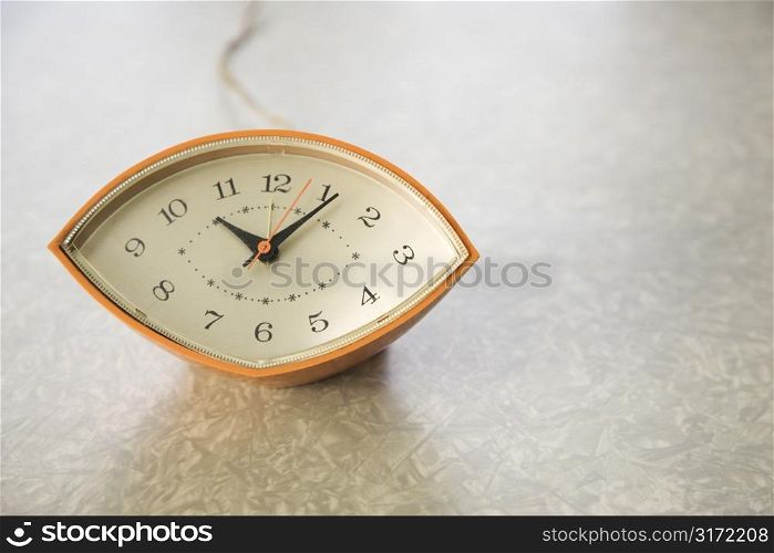 Still life of orange eye-shaped vintage clock on table.