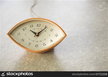 Still life of orange eye-shaped vintage clock on table.