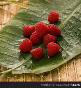 Still life of red raspberries on banana leaf.