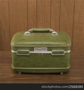 Still life shot of a vintage green luggage piece sitting on a wooden desk.