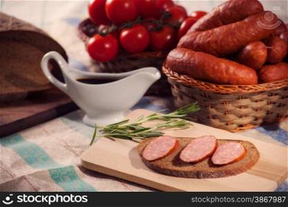 still life sliced sausage on a cutting board with rosemary, bread and tomatoes