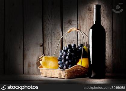 Still life with a bottle wine and basket of fruit on wooden background
