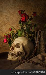 Still life with a human skull with a red rose in a vase beside the timber, and chains.