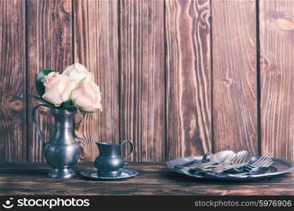 Still life with antique cutlery, plate and flowers in tin jug