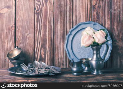 Still life with antique cutlery, plate and flowers in tin jug