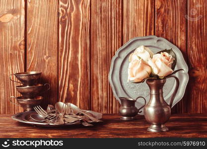 Still life with antique cutlery, plate and flowers in tin jug