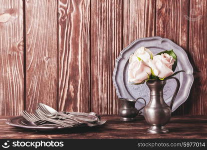 Still life with antique cutlery, plate and flowers in tin jug