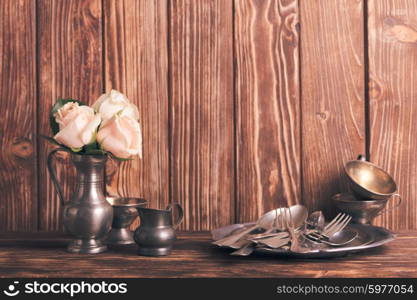 Still life with antique cutlery, plate and flowers in tin jug