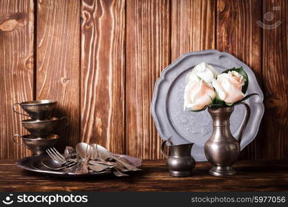 Still life with antique cutlery, plate and flowers in tin jug