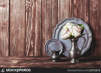 Still life with antique plate and flowers in tin jug. Vintage metal ware still life