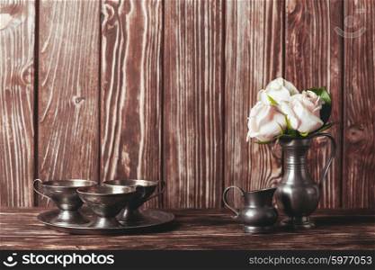 Still life with antique plate and flowers in tin jug. Vintage metal ware still life
