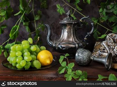 Still life with antique silver coffee pot and green grapes on a dark background