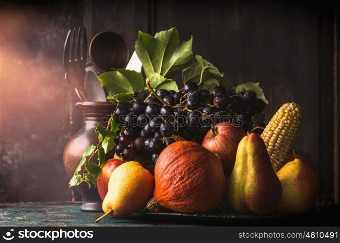 Still life with autumn fruits and vegetables: apples, pears, grapes, pumpkins, corn on the cob on dark rustic kitchen table at wooden background