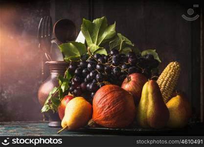 Still life with autumn fruits and vegetables: apples, pears, grapes, pumpkins, corn on the cob on dark rustic kitchen table at wooden background